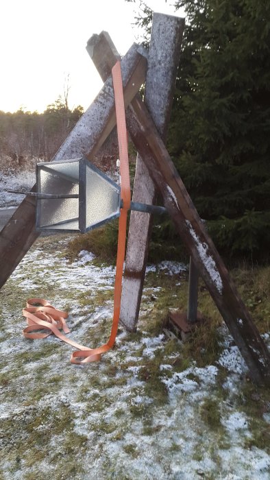 Skarvmuff i fokus uppstött med reglar och ett spännband på en snöfläckad mark med skog i bakgrunden.