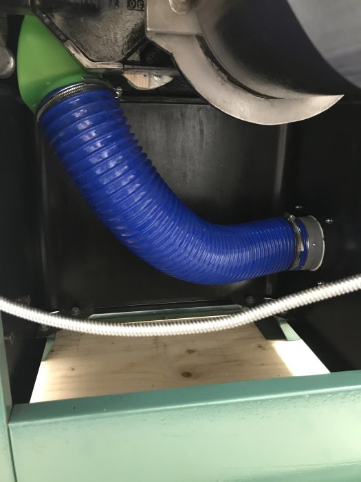 Blå flexibel 100mm-spånutsugsslang monterad i verkstadsmiljö, ansluten till maskin.