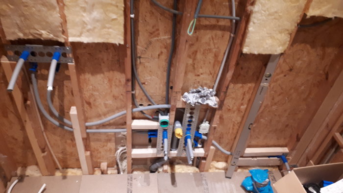Nyinstallerade rör och ledningar för VVS i en vägg under renovering med isolering och lite röran.