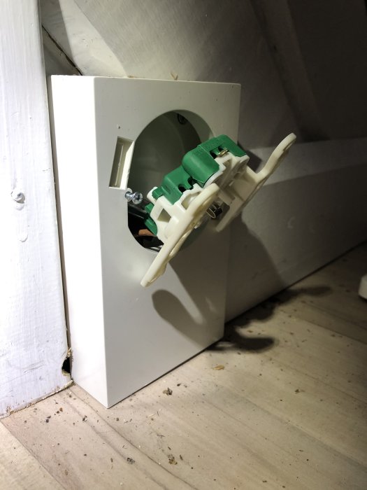 Närbild av ett öppet eluttag med en plastdistans, skruvarna synliga i djupet ej åtkomliga med mejsel.