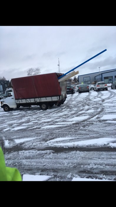 Lastbil med långt utskjutande last utan flaggning på en snötäckt parkering.