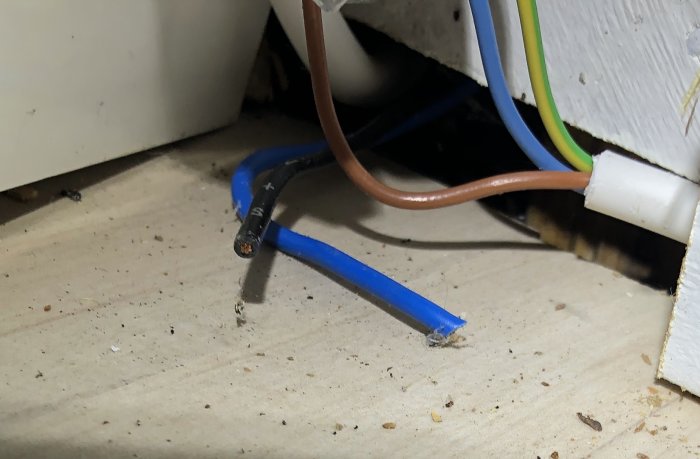 Elextriska kablar klippta nära ett vägguttag, osäker elinstallation på golvet.