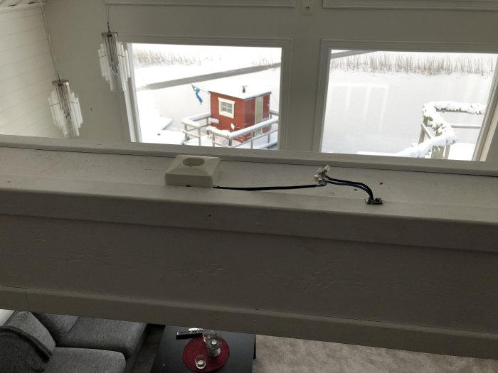 Elektrisk kabel avklippt och lämnad på fönsterkarm, bakgrund med snölandskap och röd byggnad.