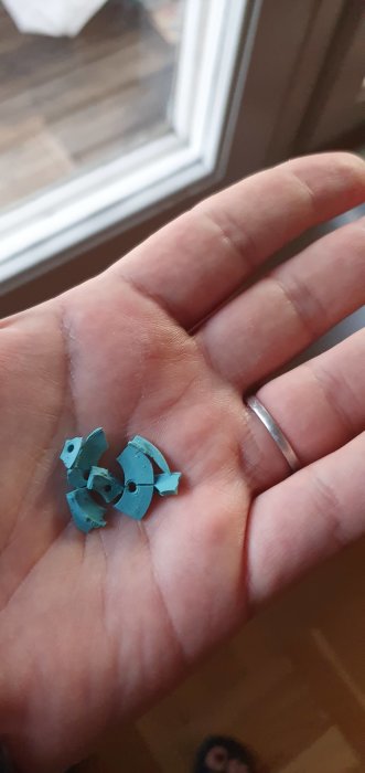 Hand visar en trasig blå plastdetalj som gäller en termostat, med suddig bakgrund.