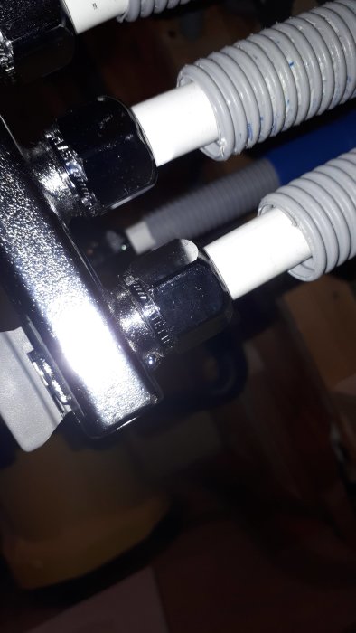 Närbild av en vit vatetteplastkoppling till en fördelare som uppvisar en läckagepunkt, monterad med synlig klämhylsa.