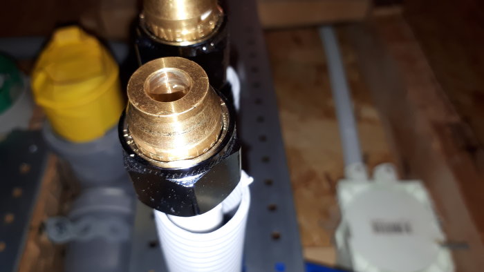 Närbild av en vatetteplastkoppling och fördelare med synlig klämhylsa i fokus, potentiellt läckande.