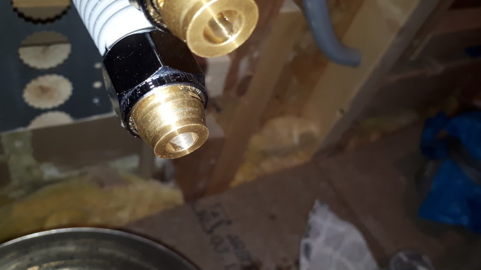 Närbild av en mässingskoppling med potentiellt materialfel, monterad på vit rörsektion.
