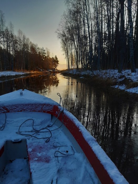 Vintermorgon i skärgården sett från en båt med snö, omgiven av träd och stilla svart vatten.