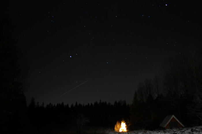 Nattbild av en upplyst gran och stjärnhimmel med ett litet rött hus i förgrunden