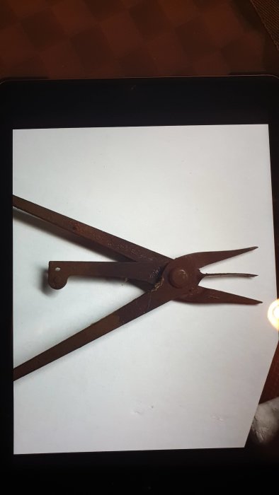 Gammal rostig metalltång med långa spetsiga armar, visas på en skärm, okänt användningsområde.
