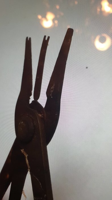 Närbild på gammal rostig tång med okänd användning mot suddig ljus bakgrund.