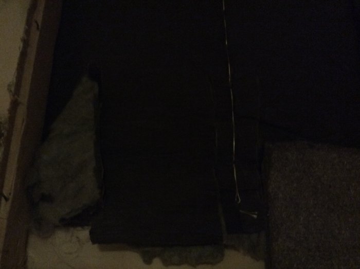 Mörk bild som visar gammal stenullsisolering bredvid mörkt vindskydd.