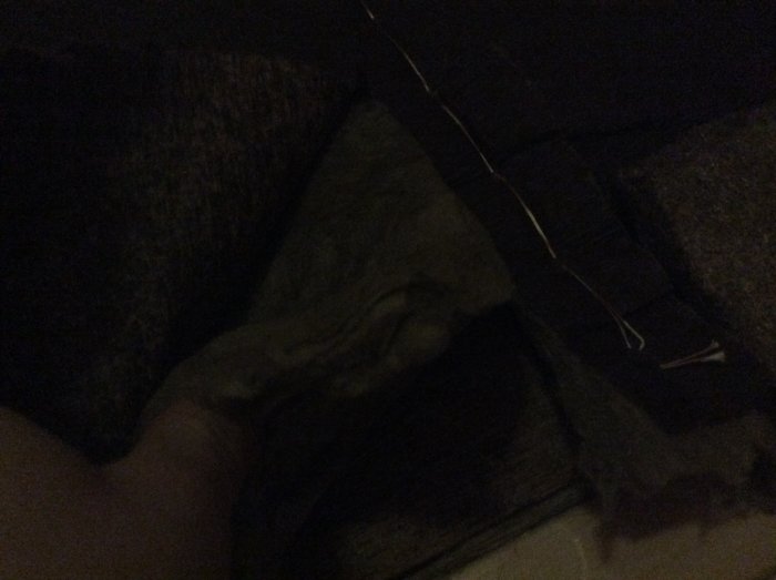 Hand håller en bit stenullsisolering med vindpapp nära en träkonstruktion.