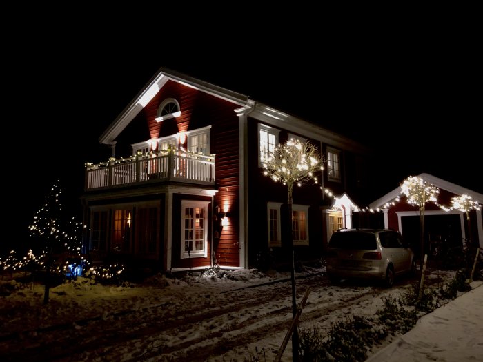 Tvåvåningshus upplyst av ljusslingor utomhus på natten, med snö på marken.