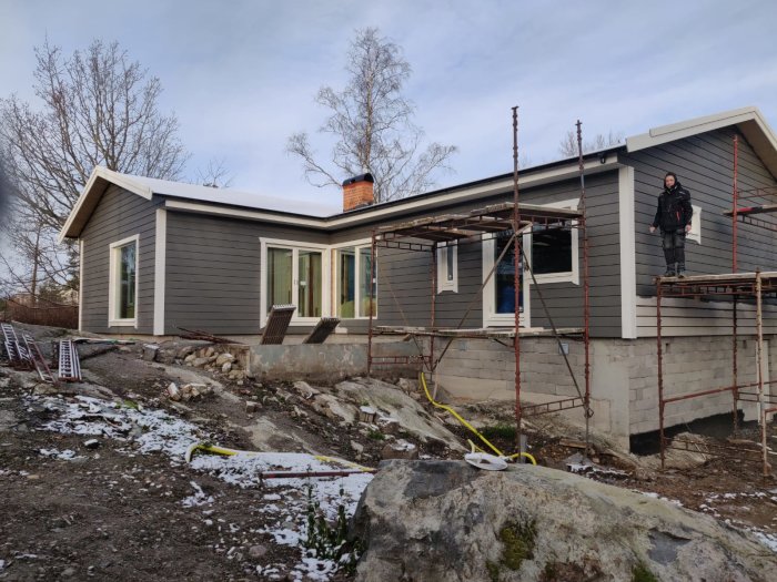 Ett hus under renovering med en person som arbetar på en byggnadsställning i vintermiljö.