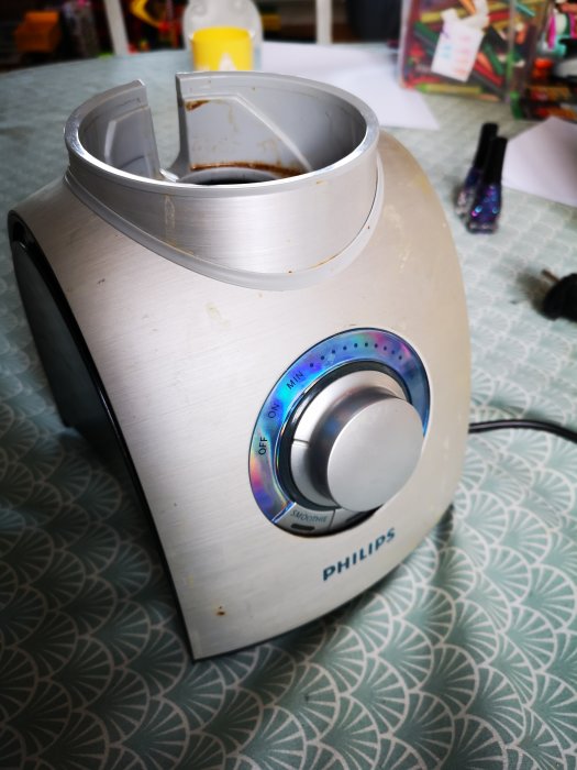 Gammal silverfärgad Philips mixer som inte fungerar, med synliga slitage och smuts, placerad på ett mönstrat bord.