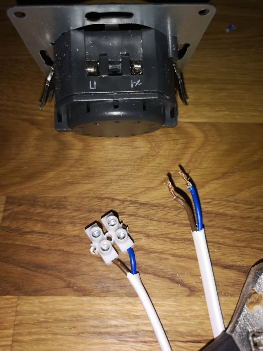 Elektrisk vägguttag utan front och isolerade elkablar med ändhylsor på ett trägolv.