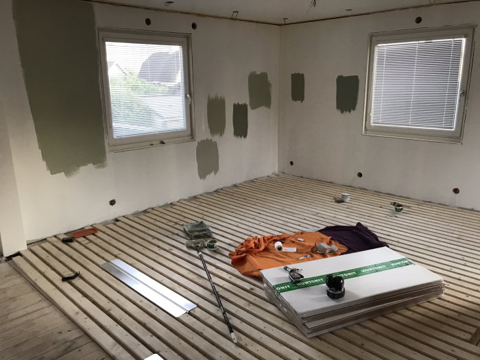 Renoveringsarbete i rum med golvbjälkar och väggtester av olika gröna färger.
