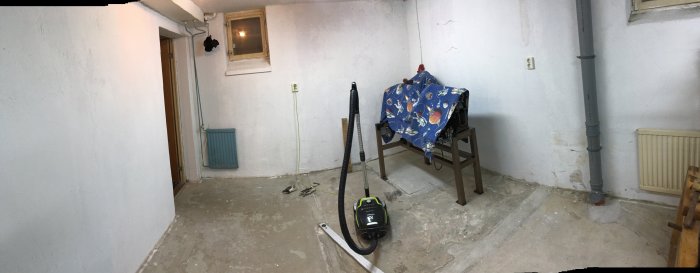 Panoramavy av ett tomt rum med ojämnt betonggolv med rester av mattlim och en maskin täckt med tyg.