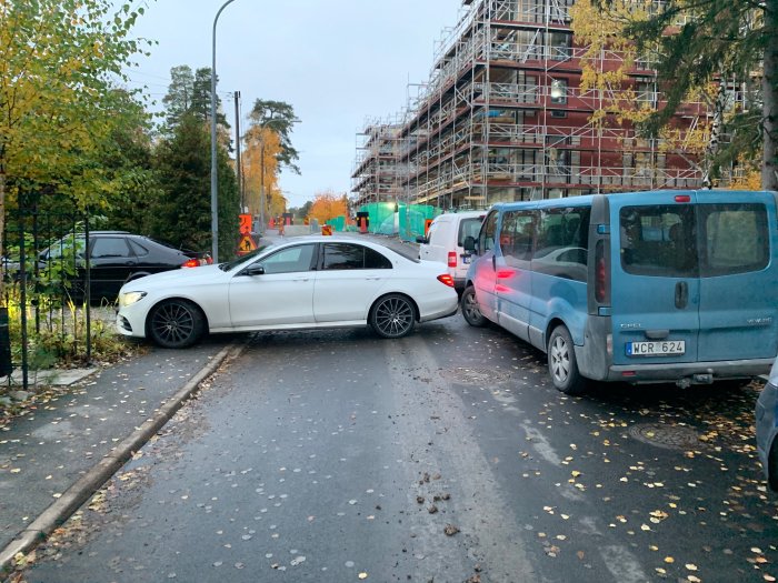 En smal gata med parkerade bilar på båda sidor och byggställningar i bakgrunden.