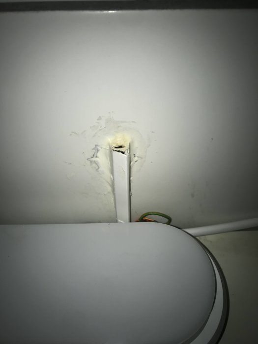 Elektrisk kabel utan jordförbindelse sticker fram ur otätad öppning i väggen ovanför toaletten.
