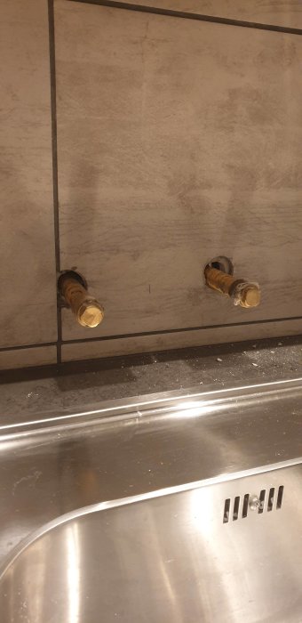 Två igensatta rör mot en kakelvägg ovanför en diskbänk i en tvättstuga redo för blandarinstallation.