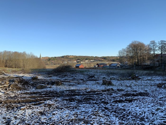 Utsikt över en dal med snöfläckar, byggnader i fjärran och en klarblå himmel.