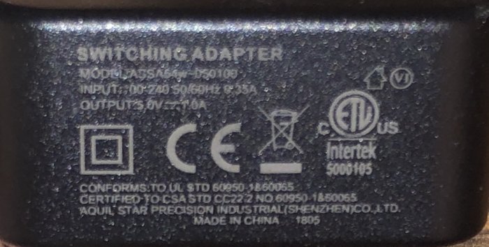 Närbild av en svart usb-adapter med text som anger modell, input/output-specifikationer och säkerhetscertifieringar.