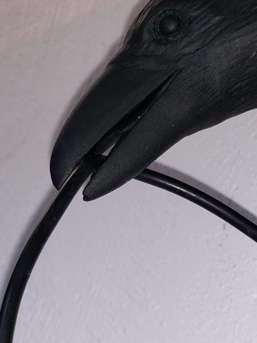 En USB-kabel som hålls av en svart fågelstatyett, indikerar trångt utrymme i näbben för större kablar.