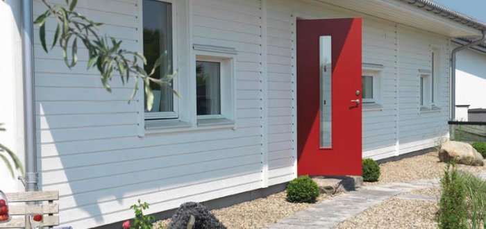 Vit villa med röd dörr och linjerade underkanter på fönster och väggpaneler.