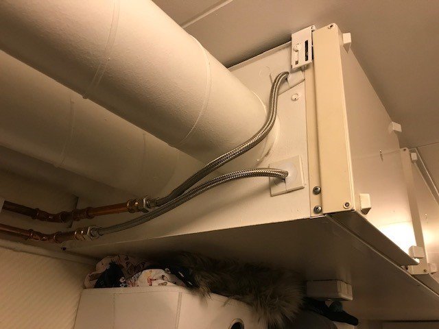 Bild på en fjärrvärmeväxlare under ett köksskåp med synliga rör och kopplingar, och fråga om var man stänger av pumpen.