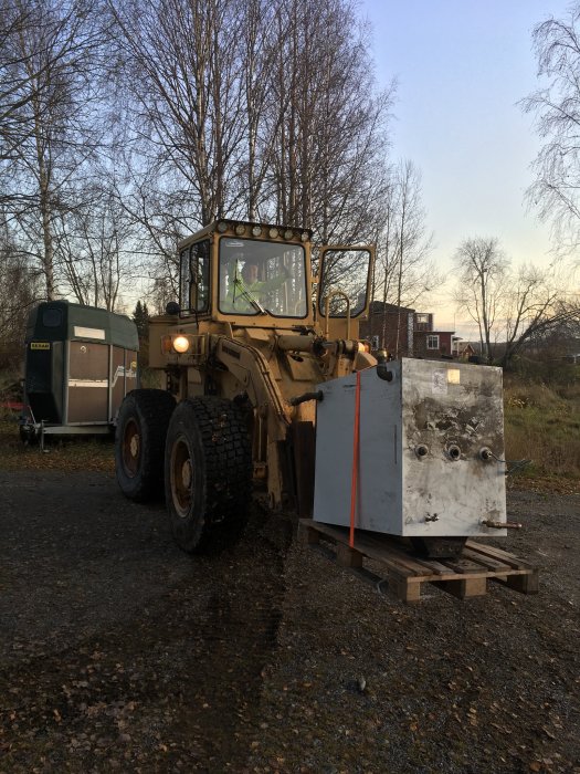 Hjullastare som flyttar en stor panna på pall i utomhusmiljö.