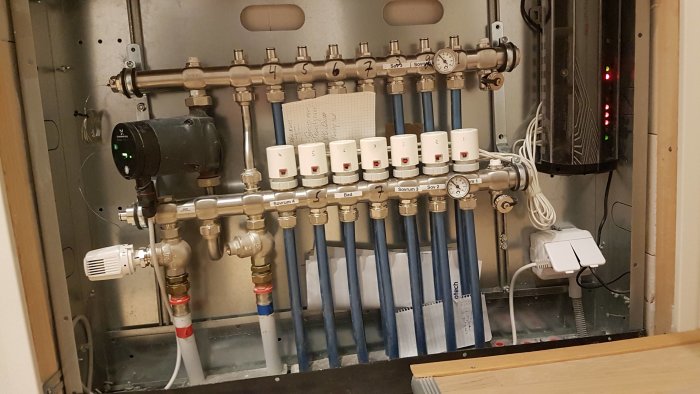 Golvvärmeinstallation med fördelarskåp, rör, termostater och pump märkt Termo tech.