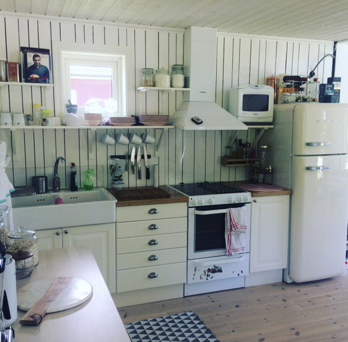 Renoverat kök med vita skåp, träbänkskiva, kylskåp och ugn, efter projektets slutförande.