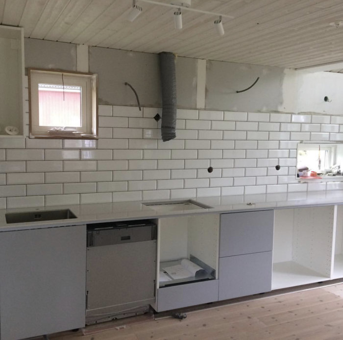 Kök under renovering med omonterade skåpluckor och vitt kakel på väggen, arbetsytan ännu ej installerad.