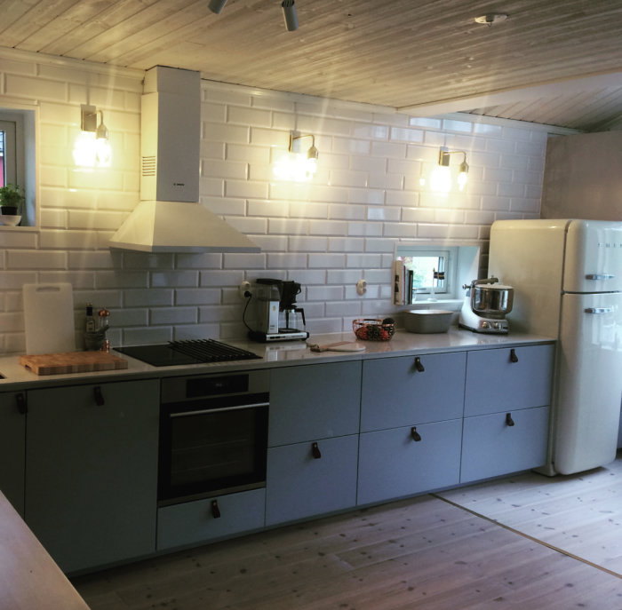 Nyrenoverat kök med ljus kakelvägg, blå skåp och vitvaror, efter avslutat 4-dagars byggprojekt.