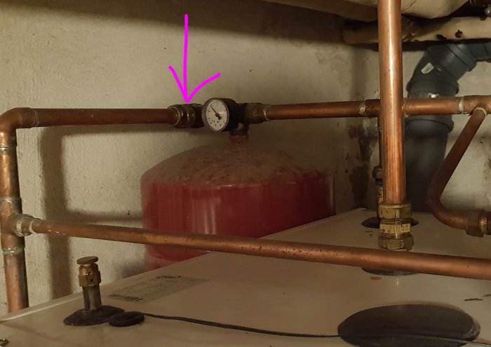 Säkerhetsventil för värmesystem markerad med lila pil ovanför expansionskärl och rörinstallationer.