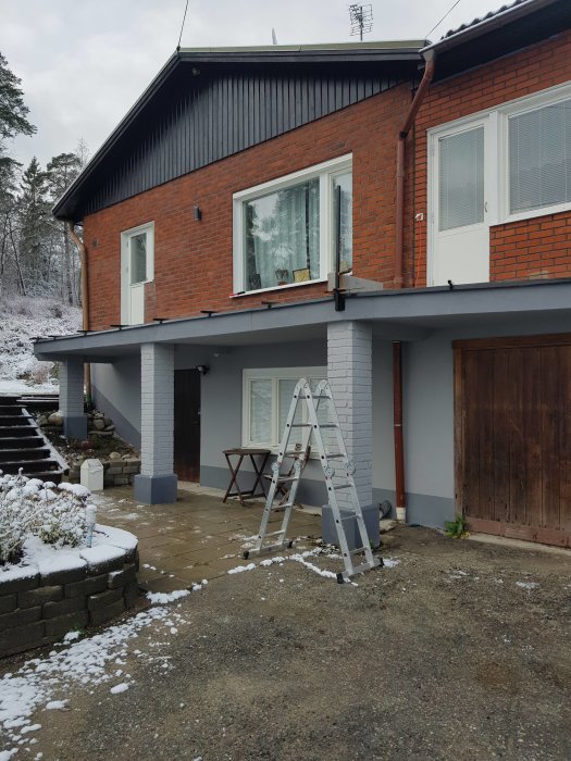 Nyrenoverat garage under snötäckt tak med stege framför och bostadshus i bakgrunden.