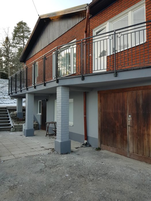 Nyinstallerade grå pelare under balkong på rödtegelhus med garageport.