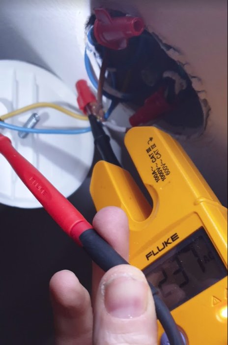 Hand håller en Fluke multimeter som mäter elektrisk spänning i en eldosa under installation.