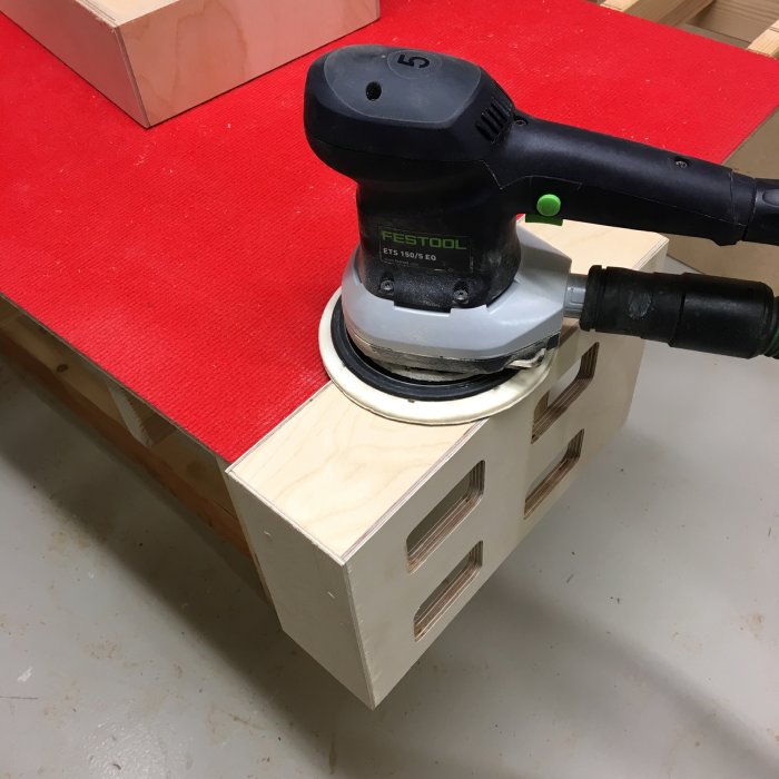 Slipmaskin från Festool används för att släta till ytan på en plywoodlåda under förberedelser inför montering av gångjärn.