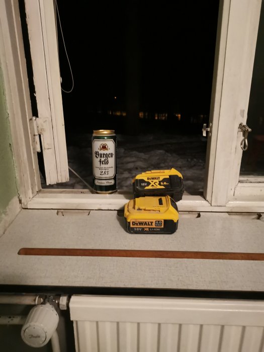 En Dewalt-batteriladdare och -batteri på ett fönsterbleck med en ölburk, nattutsikt utanför fönstret.