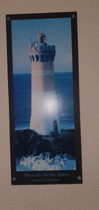 En tavla på en vägg som framställer fyren Phare des Pierres Noires omgiven av havsvågor, monterad med skruvar.