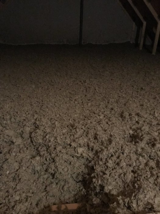 Oisolerad vind med lösullisolering och framgrävd bjälke, i ett mörkt och oinrett utrymme.