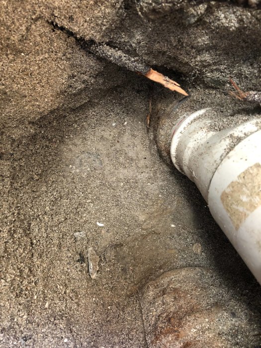 Gammalt gjutjärnsrör anslutet till betongrör under källargolvet, synlig skarv och omgivande mark.