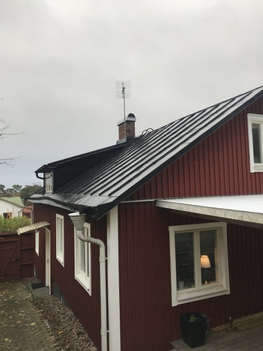 Gammaldags ståndfalsat plåttak på röd stuga, nyligen målat men med potentiell läckagepunkt.