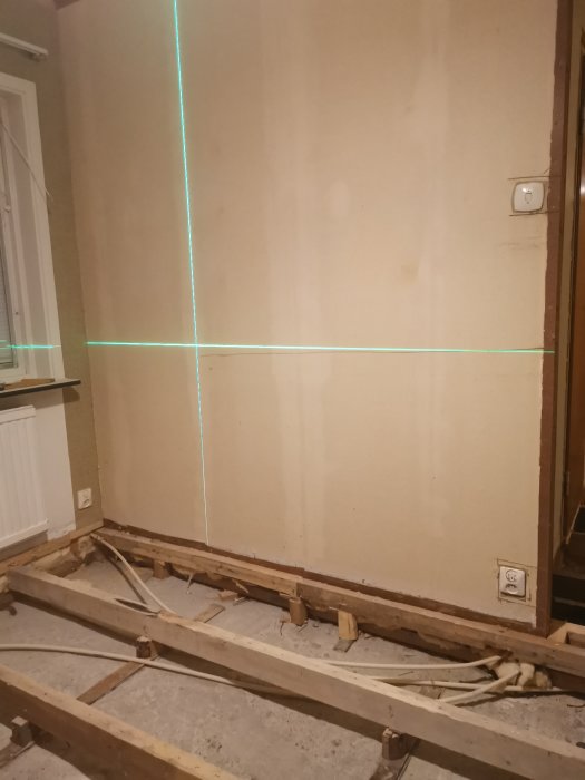 Renovering av vägg med laserlinjer som guidar kapning, synligt vägguttag och golvrörelse.