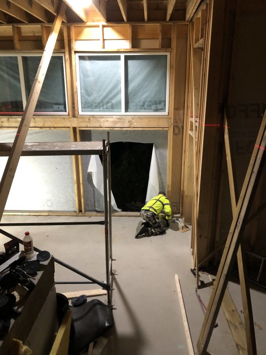 Interiör av en byggarbetsplats med halvt installerade fönster på en trävägg, konstruktionsmaterial och en arbetare.