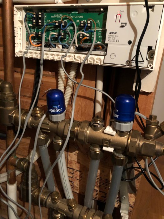 Öppen värmeväxlare med kopparledningar, Uponor-styrdon och elcentral utan märkning.