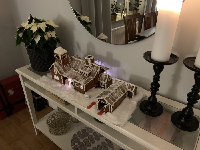 Pepparkakshus som liknar användarens hem, på ett bord dekorerat till jul med ljusstakar och julstjärna.
